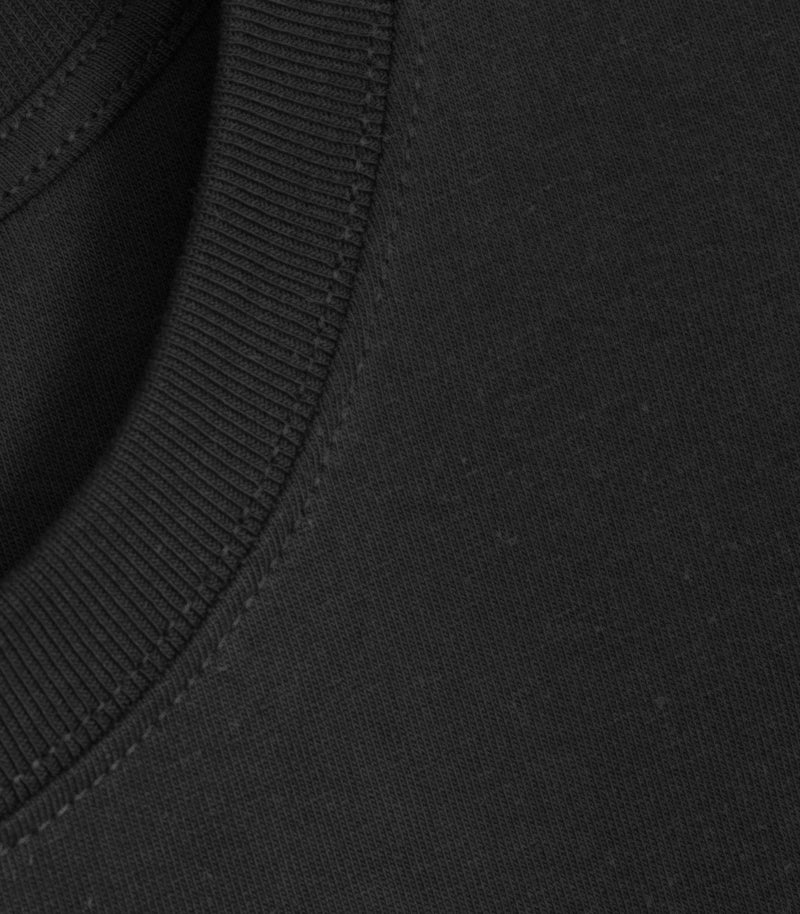 Close-up product view of a black crewneck t-shirt, showcasing the tight knit texture of the premium cotton jersey fabric, the fine structure of the ribbed collar, and precise tonal topstitching along the neck seam.
