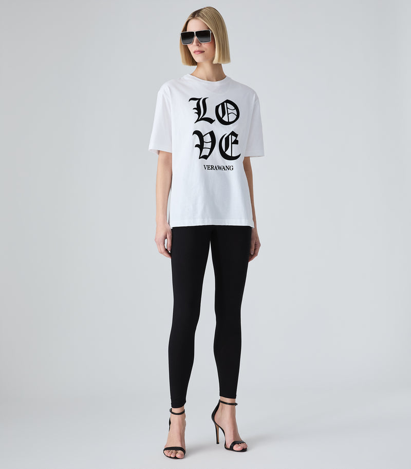 Female model wearing a white t-shirt with 'LOVE VERA WANG' spell-out logo across the front, paired with black leggings, sunglasses and heels, against a white background.
