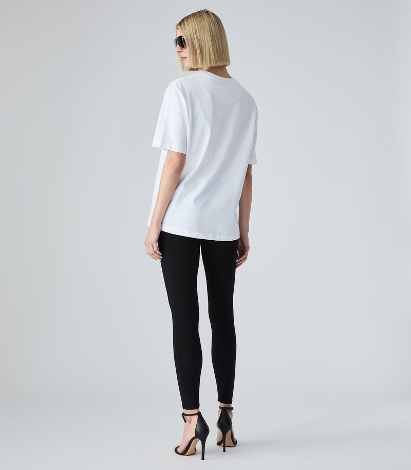 Female model wearing a white t-shirt paired with black leggings and sunglasses, against a white background.
