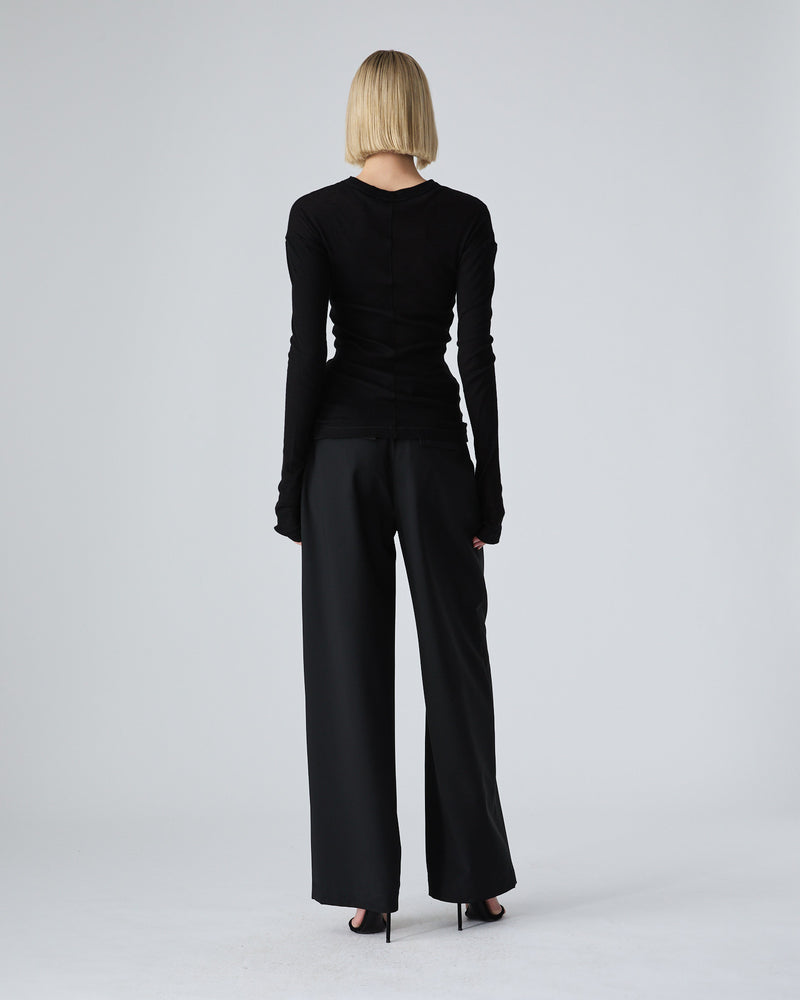A model from behind wearing a black long-sleeve top and black wide-leg trousers, standing against a light gray studio background.