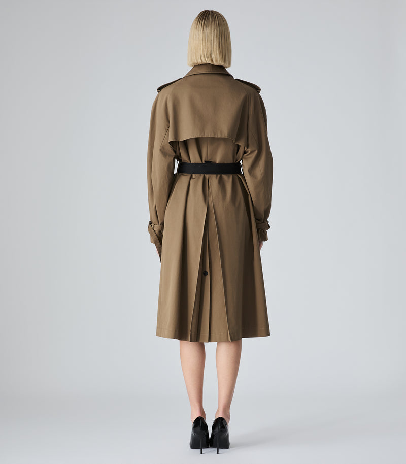 A model viewed from the back wearing a classic brown trench coat with a black belt, paired with black heels, against a light gray studio background.