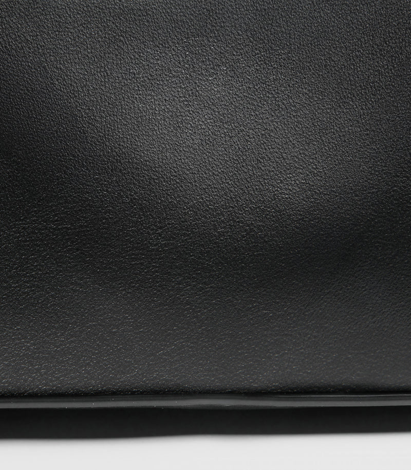 Close-up of a black textured leather bag with a thin dark horizontal edge against a white background.