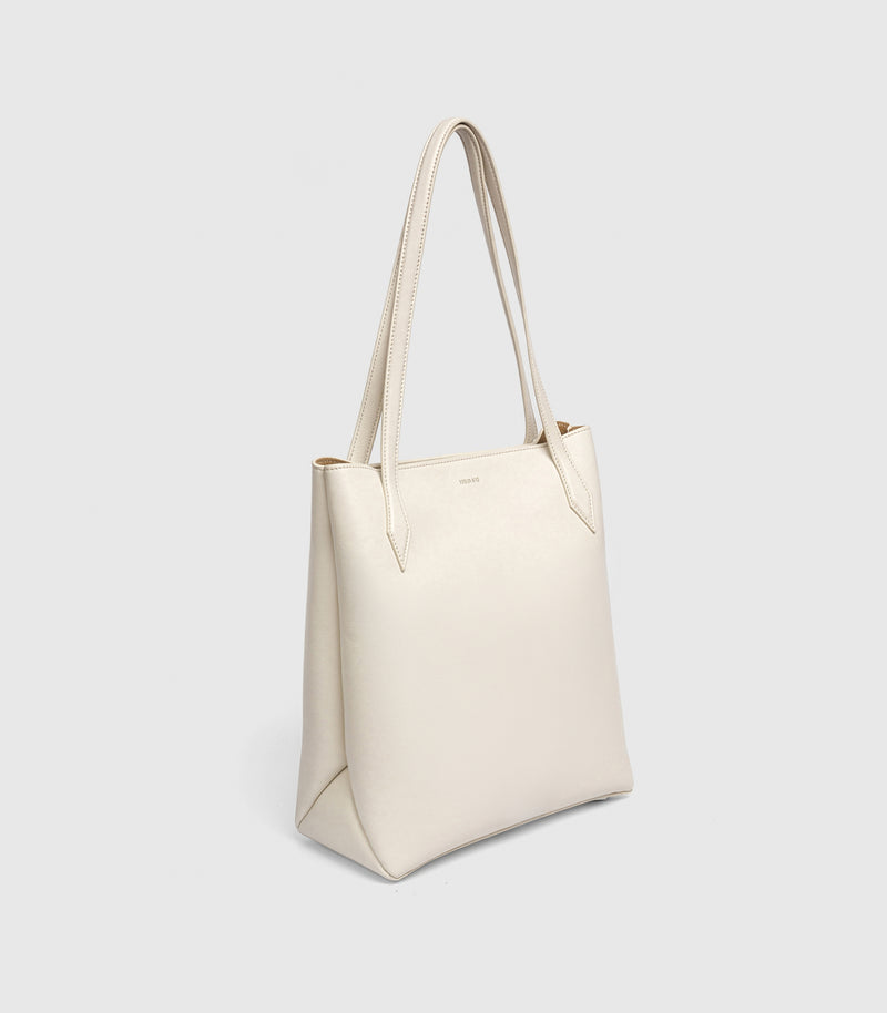 An off-white leather tote bag with double shoulder straps, shown from a three-quarters angle against a light gray background.