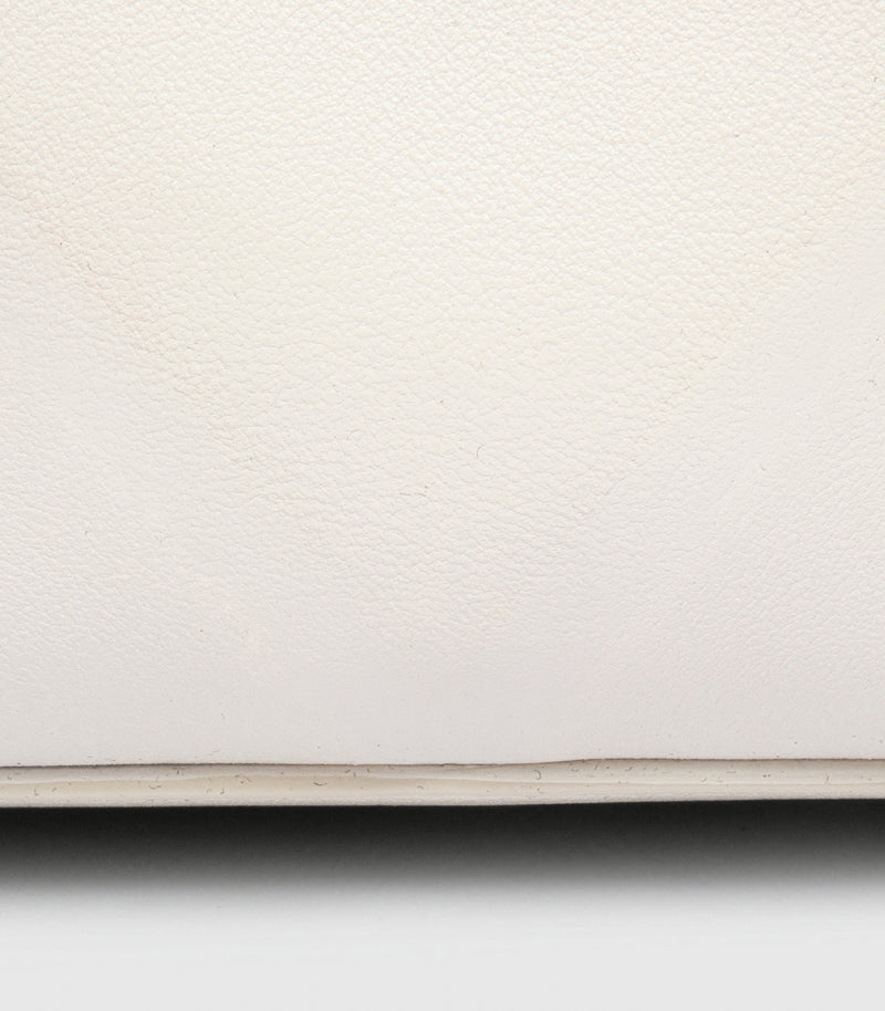 A close-up of a off-white leather bag with a thin horizontal edge and a dark shadow below.