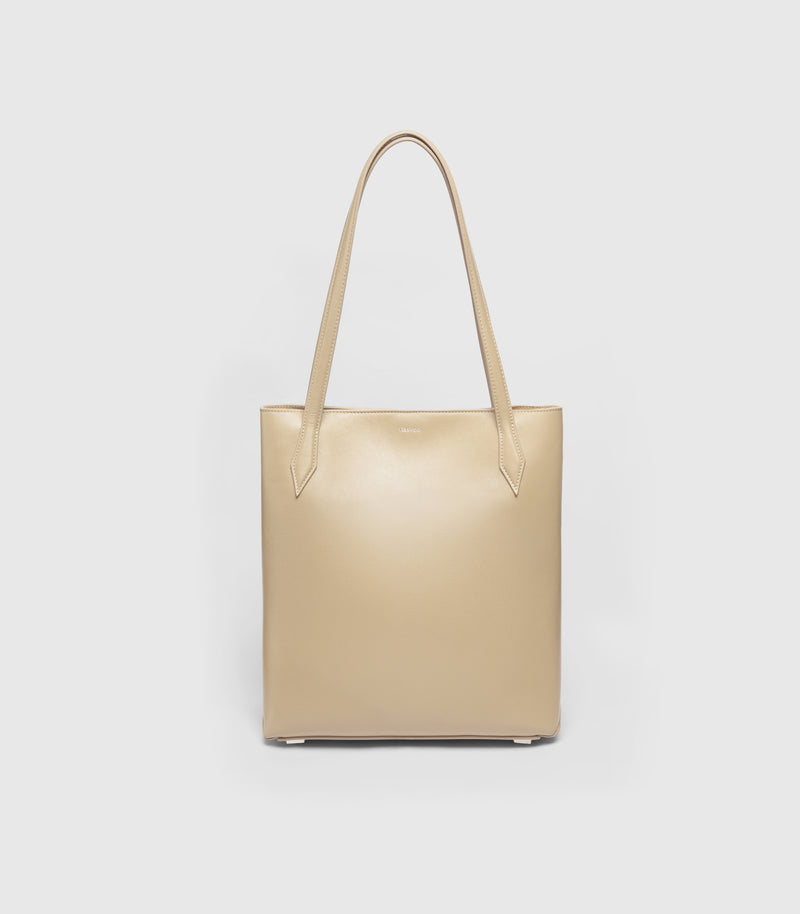 A structured beige leather tote bag with long shoulder straps, shown against a plain light gray background.