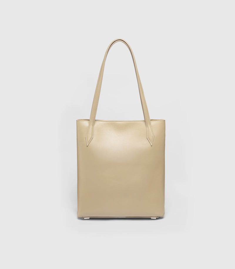 A structured tote bag in a light beige or champagne color, featuring two shoulder straps and a smooth leather-like finish, shown against a plain light gray background.