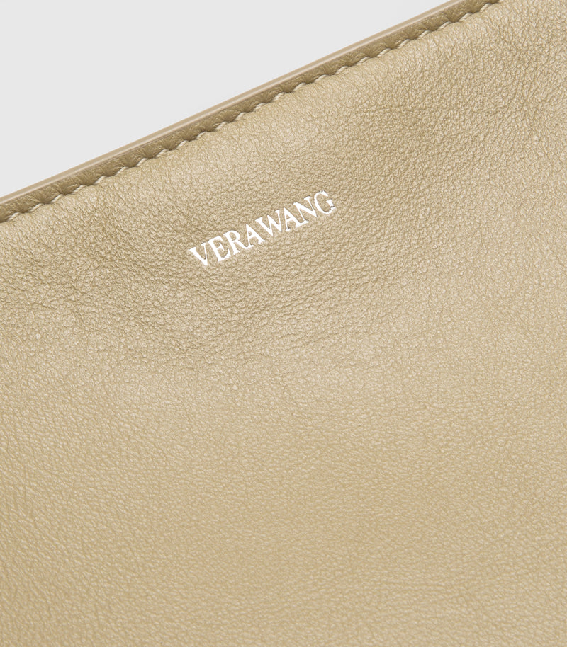 Close-up of a beige leather tote with the brand name 'VERA WANG' embossed on the front, showing fine grain texture and a matching leather zipper edge.