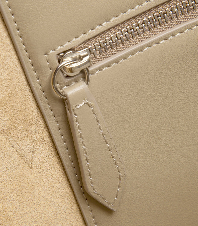 Close-up of a beige leather zippered pouch with a matching leather pull tab and silver-tone metal hardware.