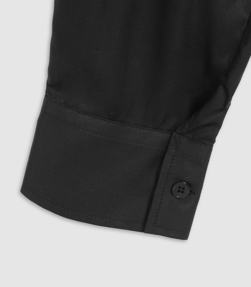 Close-up of a black long-sleeve shirt cuff showing the buttoned placket and fabric texture against a light gray background.