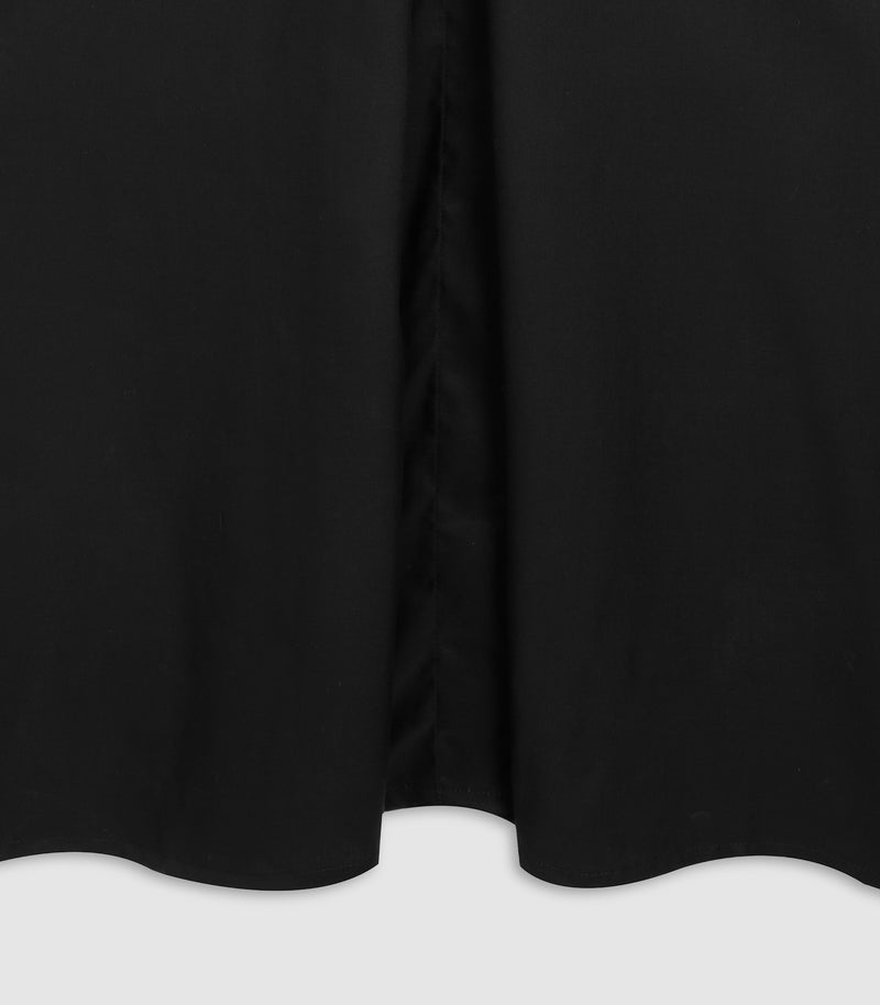 Close-up of a black garment, likely a dress or long skirt, showing a gathered center seam and scalloped hem against a light gray background.