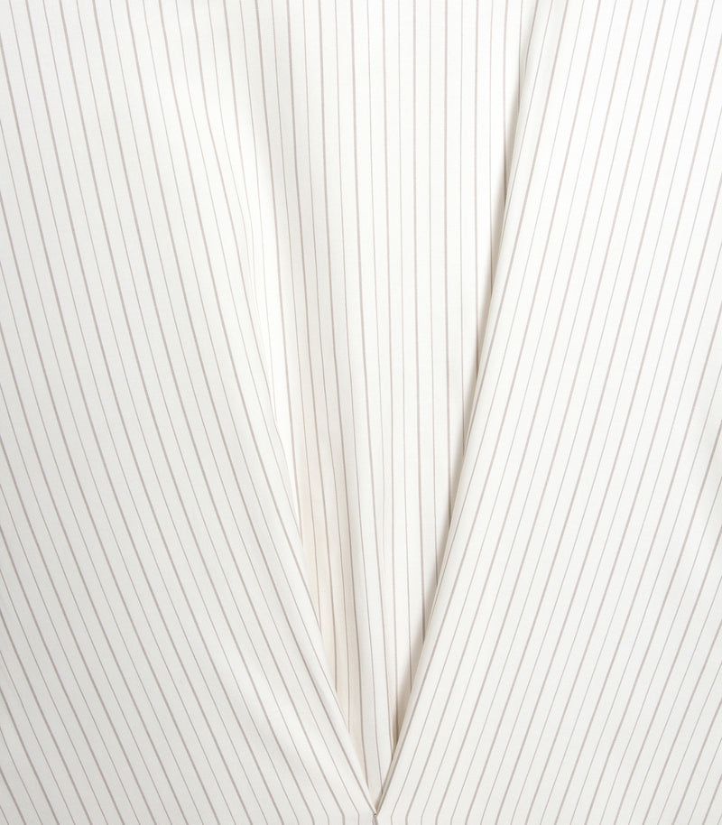 An extreme close-up product view of an ivory and beige pinstripe shirt dress, highlighting the architectural fabric manipulation. The image focuses on the point where the panels intersect, showing how the clean vertical pinstripes of the central section contrast sharply with the angled, bias-cut stripes of the structural front drapes that converge into a crisp V-shaped fold.