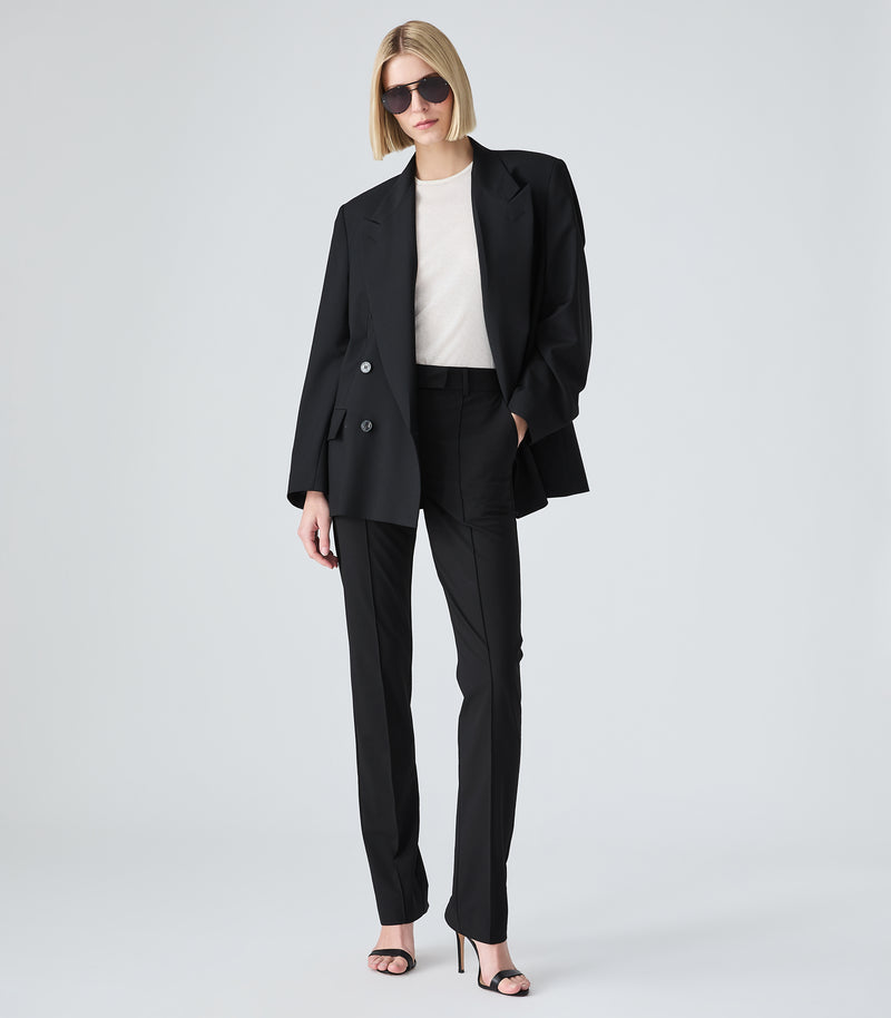 Woman wearing a black suit with a white shirt on a light gray background