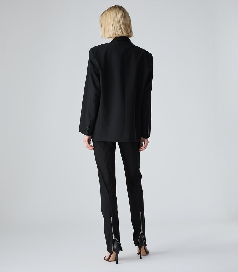 Person wearing a black suit on a plain background