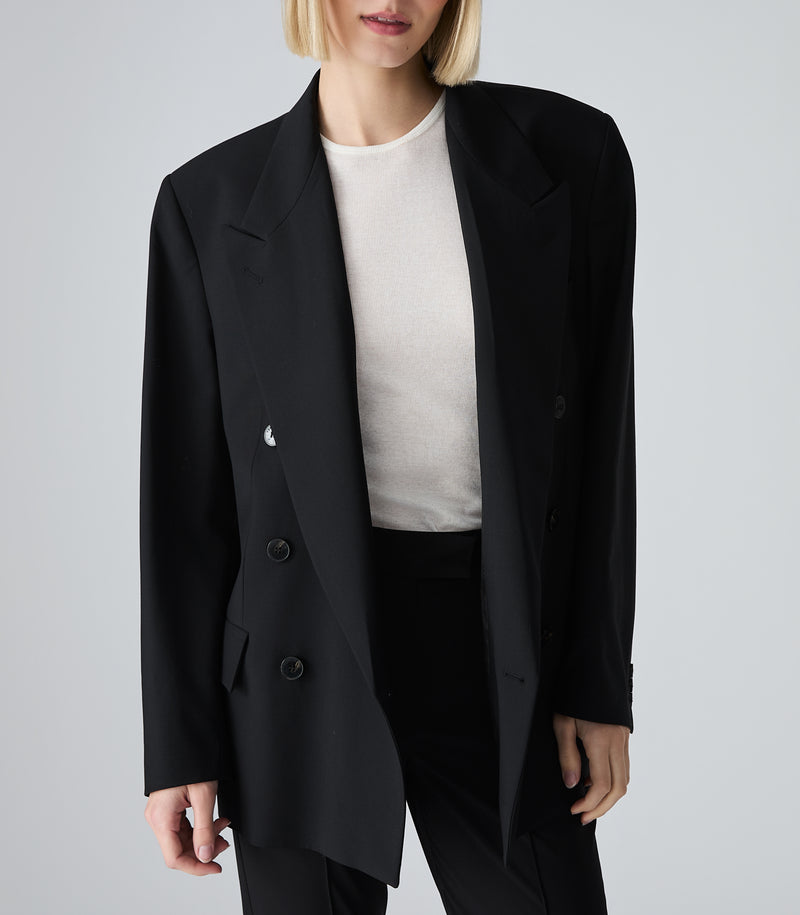 Person wearing a black blazer over a white shirt on a gray background