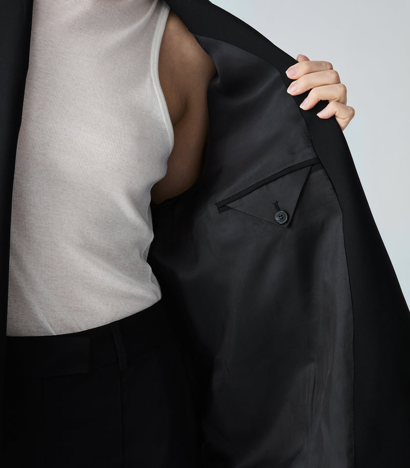 Person wearing a black jacket over a white shirt against a light gray background
