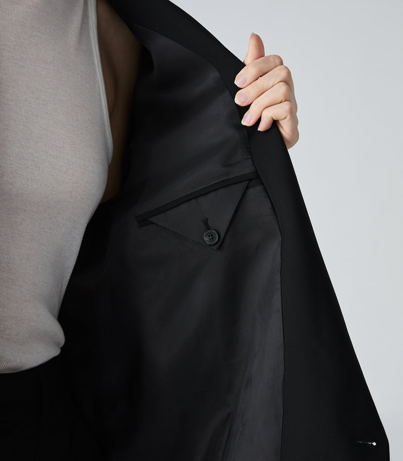 Person wearing a black coat with a gray shirt underneath on a light gray background