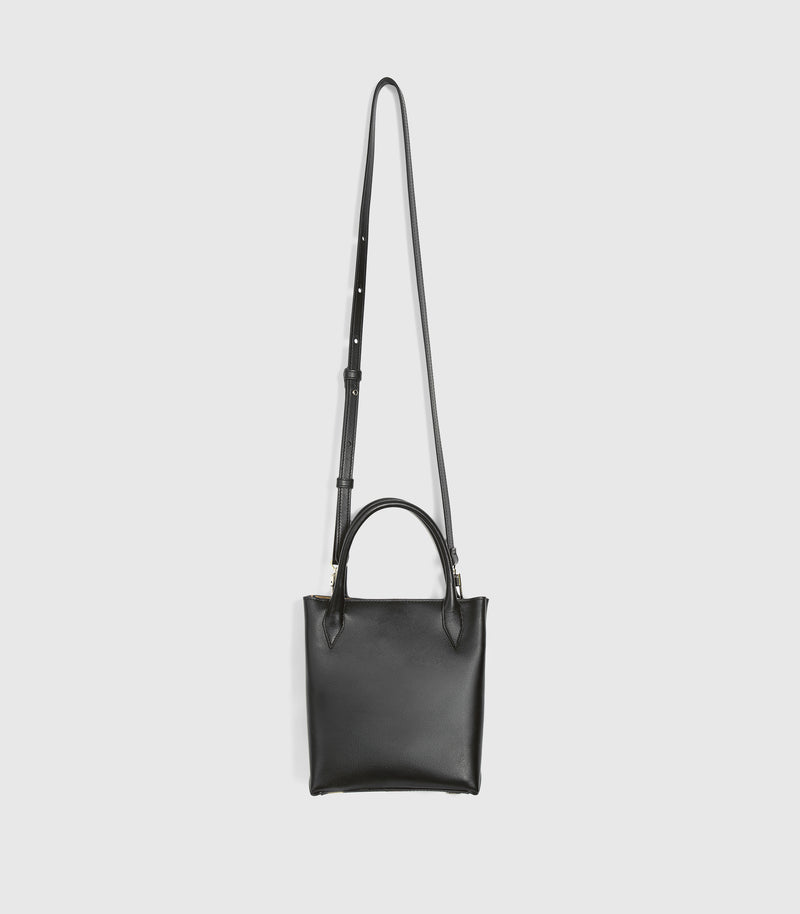 A black leather crossbody handbag with a top handle and a long adjustable shoulder strap, shown against a light gray background.