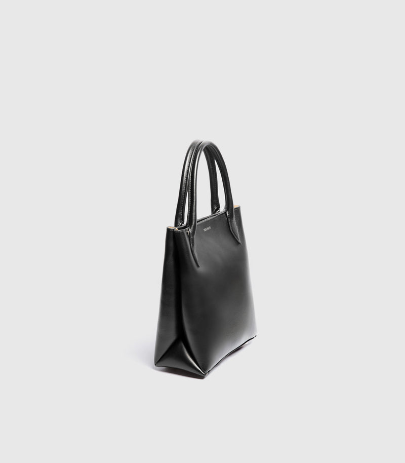 Side angle of a Black leather tote handbag with the double handled detailing against a white background