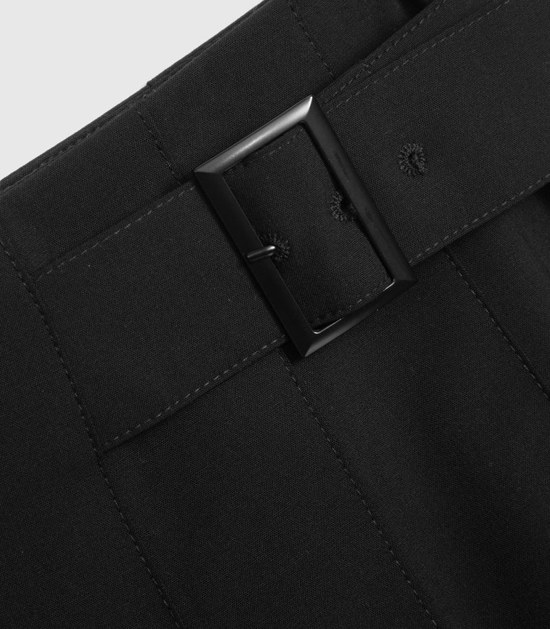 Close-up detail of a black skirt showing the belt loop, belt buckle, and stitched waistband.