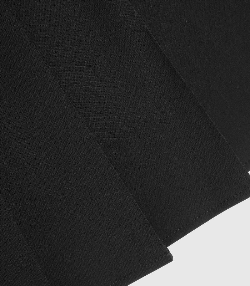 A close-up of black skirt with diagonal folds and visible stitching along the edges, set against a light gray background.