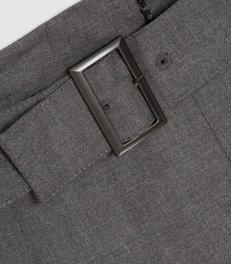 Close-up of dark gray textured trousers showing a large rectangular dark metal belt buckle, belt loop, and zipper detail.
