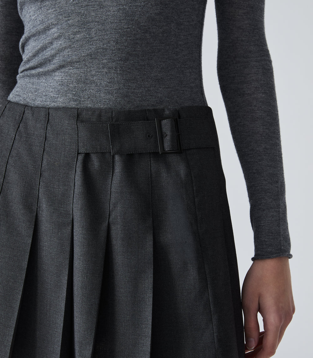 Close-up of a person wearing a dark charcoal gray pleated skirt with a matching belt and a heather gray long-sleeve top, shown against a light gray studio background.