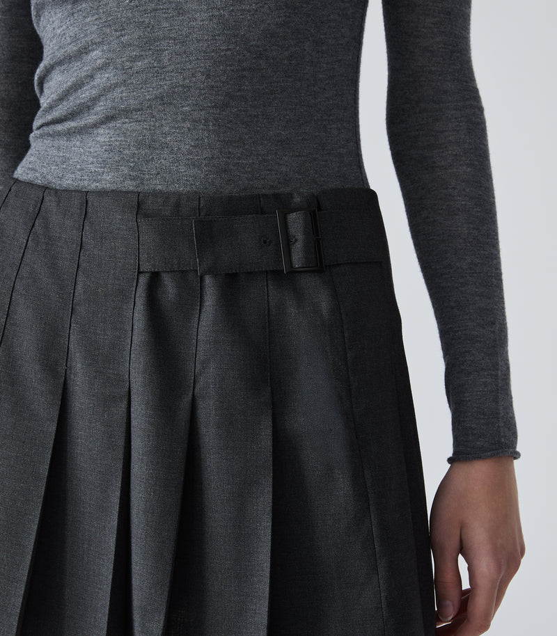 Close-up of a person wearing a dark charcoal gray pleated skirt with a matching belt and a heather gray long-sleeve top, shown against a light gray studio background.