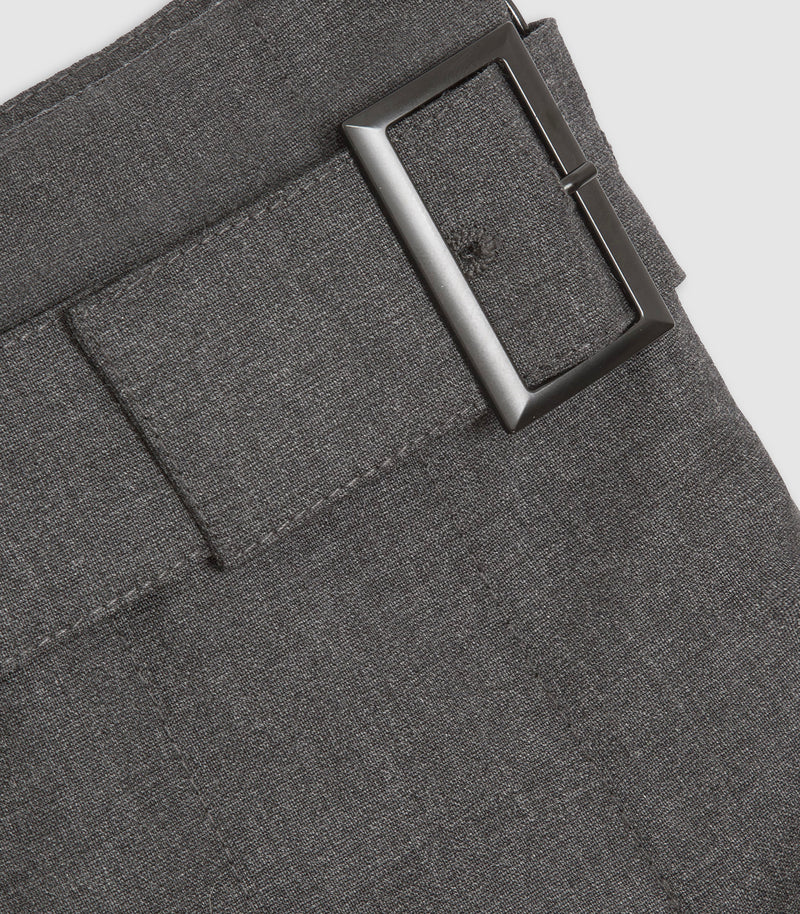 Close-up of dark gray textured trousers showing the waistband, belt loop, and a dark metallic rectangular buckle on a light gray background.