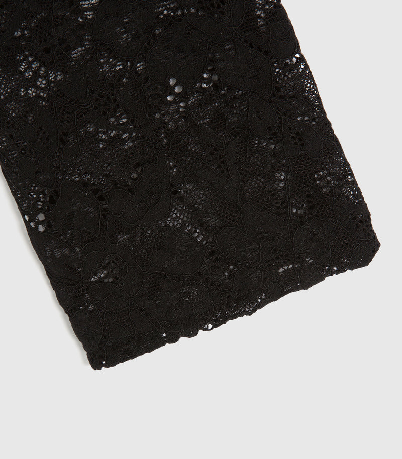 Macro close-up product view of a long-sleeved top's sleeve cuff, showcasing the intricate webbed structure and semi-translucent quality of the black floral lace fabric. The image highlights a clean, raw-edge stitched wrist hemline, detailing the fine mesh patterns and delicate leaf motifs of the textile against a light grey background.