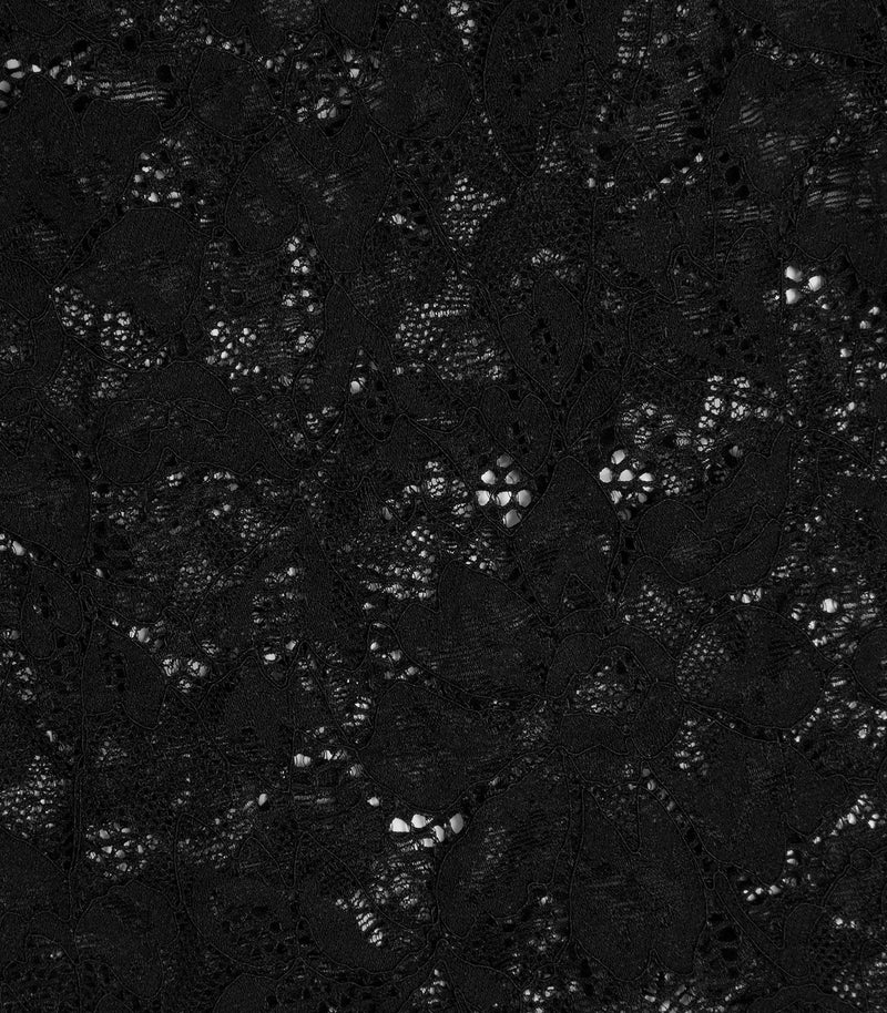 An extreme close-up of a premium black floral lace fabric, highlighting the intricate textile design. The shot showcases the delicate contrast between the densely woven, solid leaf and petal motifs and the openwork, semi-translucent mesh netting that forms the background of the lace pattern.