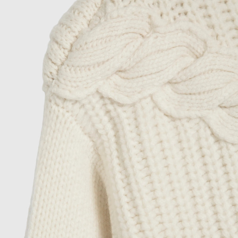 Close-up of a cream-colored cable-knit sweater showing the detailed knit texture and shoulder cable pattern against a white background.