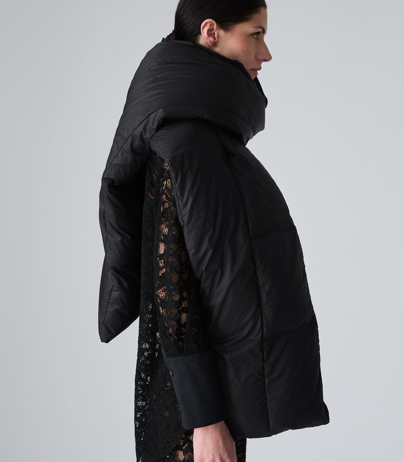 A model shown from the side profile wearing a black puffer jacket with a high padded collar and black lace sleeves, set against a plain light gray studio background.