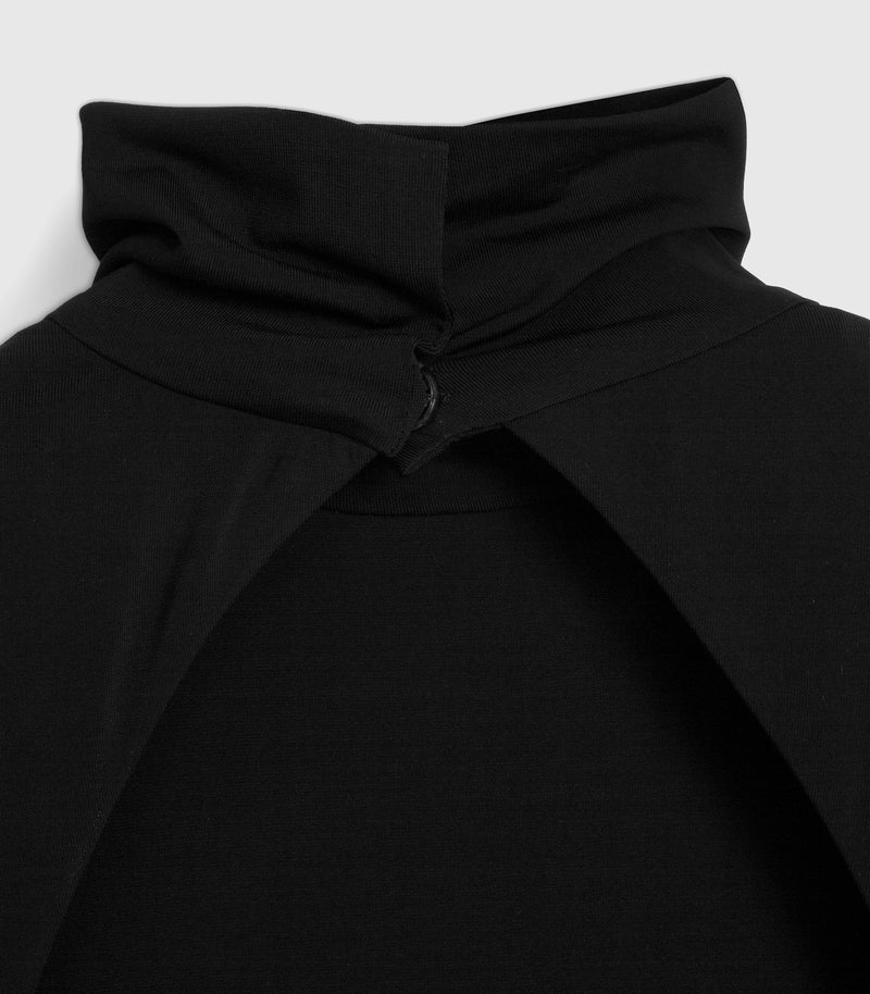A macro close-up product view focusing on the rear neckline fastenings of a black maxi dress. The image highlights a high funnel neck collar made from smooth matte jersey, which features an elegant fabric overlap secured at the nape with a subtle, fabric-covered button closure. Below the fastening, the clean-cut edges separate smoothly to begin the dramatic open-back architectural curvature, shot against a light grey background.