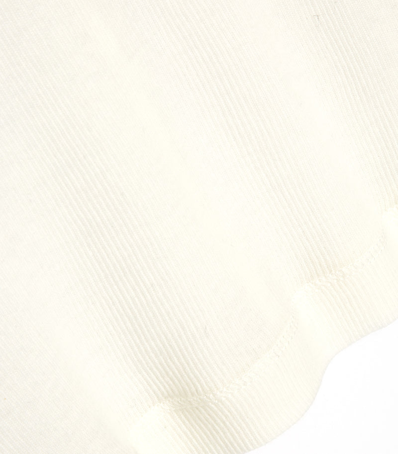 An extreme close-up detail of the hemline on an ivory white sheer jersey top from Vera Wang. The macro shot emphasizes the delicate, fine-ribbed fabric texture and the clean stitched edge of the lightweight garment.