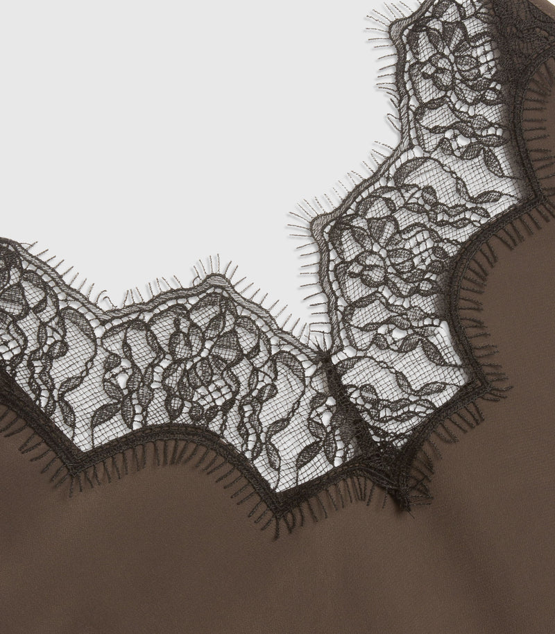 Close-up of a beige garment featuring a wide, scalloped black lace neckline with delicate mesh and floral embroidery.