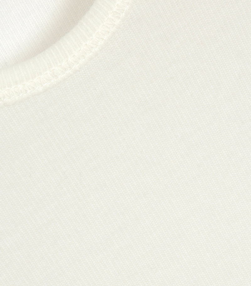Macro close-up view of an ivory tank top, highlighting its soft, fine-gauge vertical ribbed-knit texture. The shot focuses on the clean, reinforced topstitching running along the narrow ribbed binding of the neckline and armhole borders.