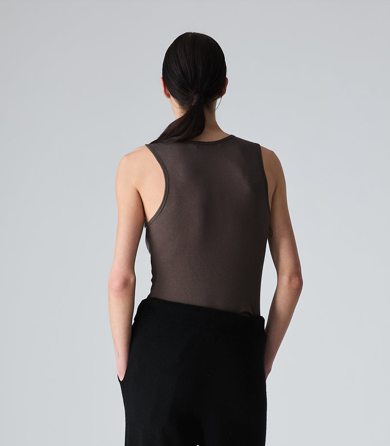 A model shown from the back wearing a dark brown sheer mesh sleeveless top and black pants, set against a plain light gray studio background.