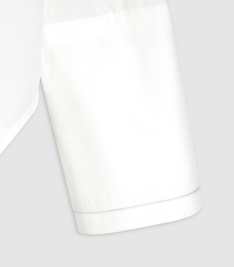 Close-up of a white fabric garment sleeve or cuff with visible stitching and a folded hem, photographed on a light gray background.