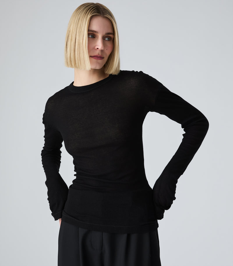 A blonde model wearing a black long-sleeve crewneck knit top, posed against a light gray studio background.