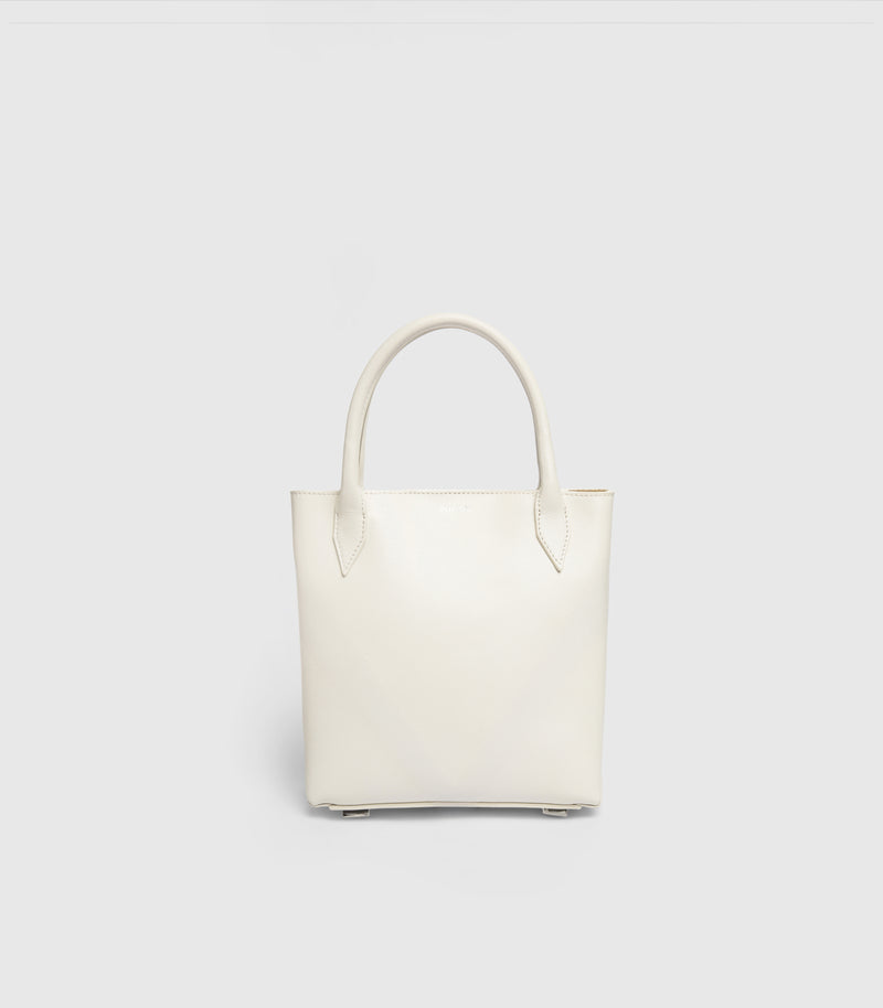 A minimalist off-white leather tote bag with double top handles, shown against a solid light gray background.