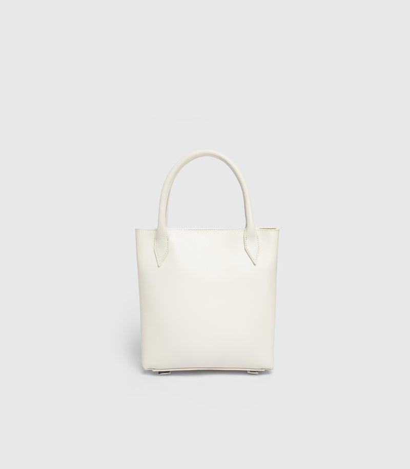 A minimalist off-white leather tote bag with double top handles, shown against a solid light gray background.