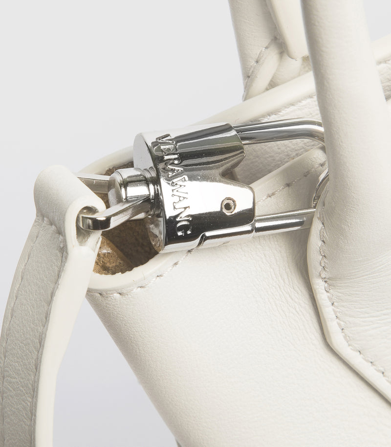 Close-up of a white leather handbag featuring a silver padlock-shaped metal clasp with the brand name 'VERA WANG' engraved on it.