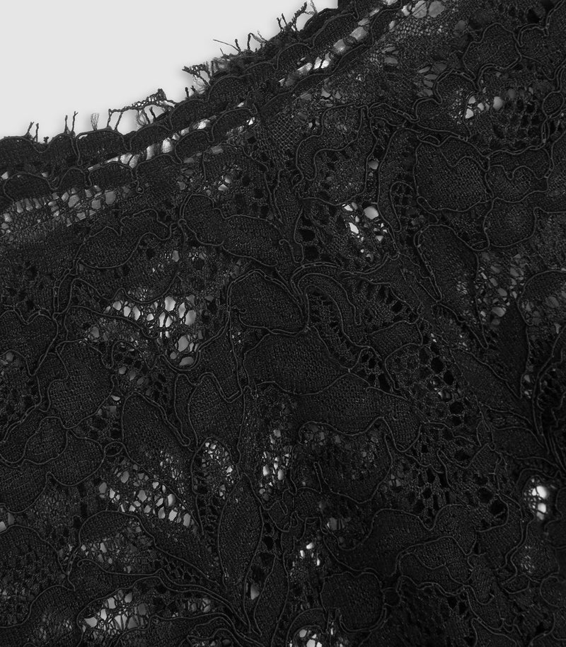 Close-up of black lace fabric with floral and leaf patterns, showing the detailed mesh and embroidered texture against a light background.