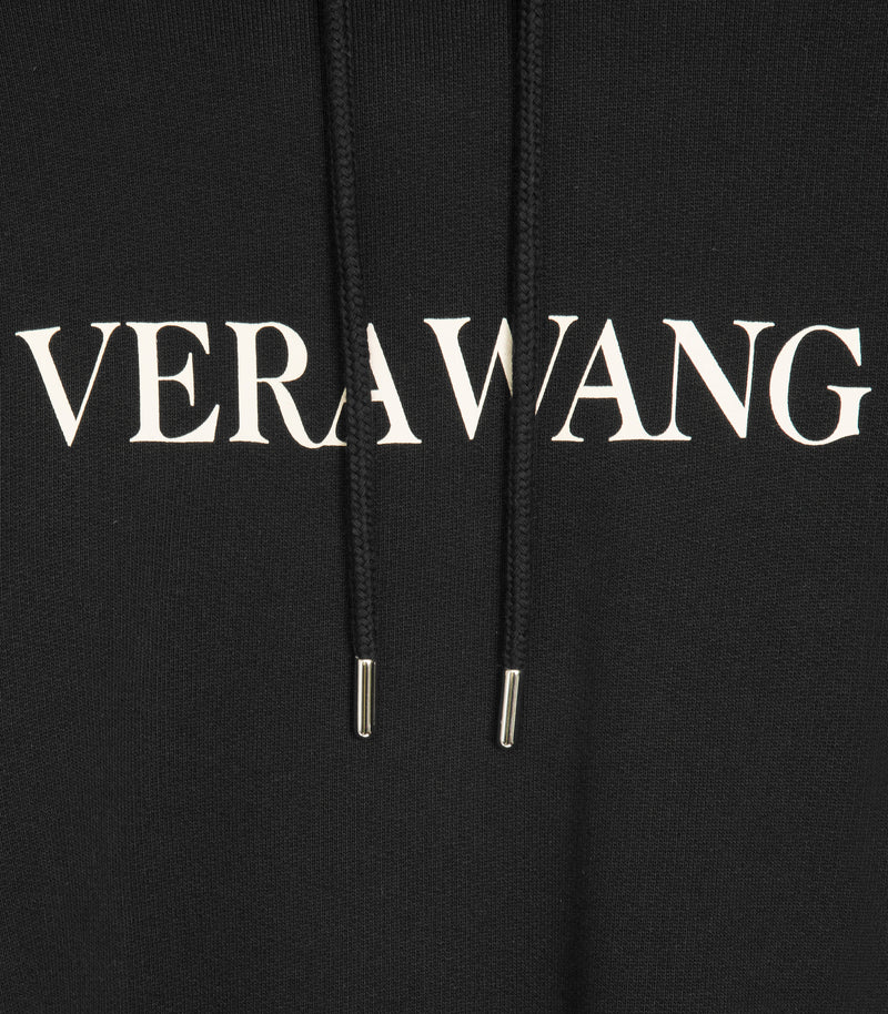 A detailed shot of the white 'VERA WANG' spell-out logo across the chest, with the hoods drawstrings draped over it.