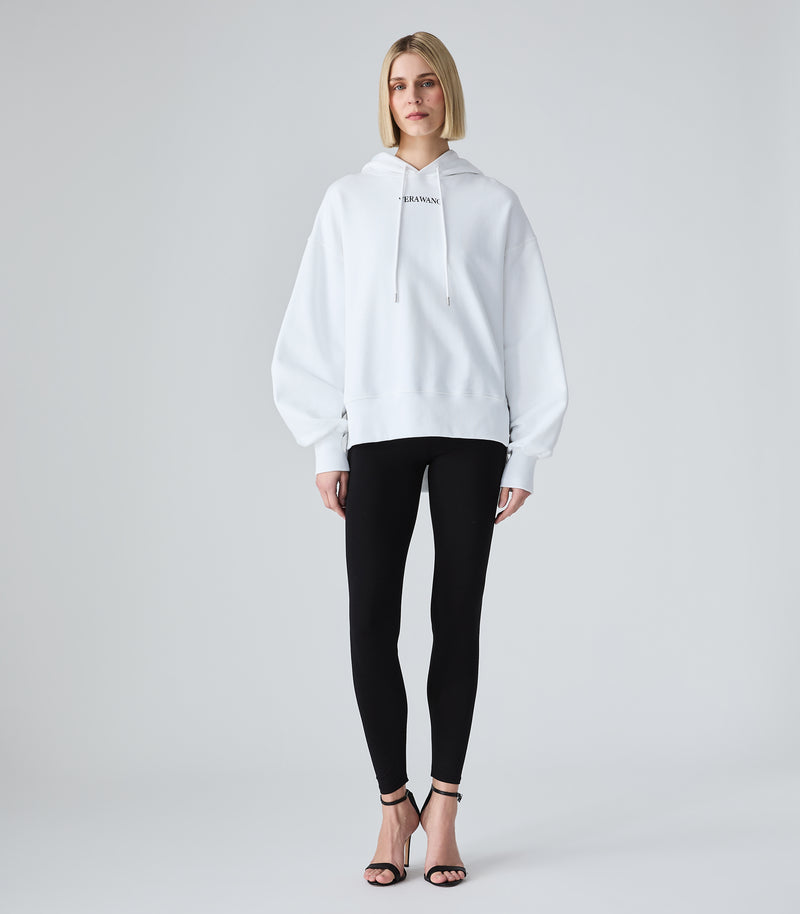 A model wearing a white oversized pullover hoodie with a small black 