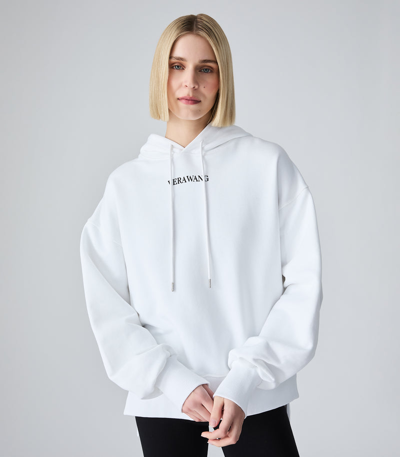 A blonde model wearing a white pullover hoodie with a black 