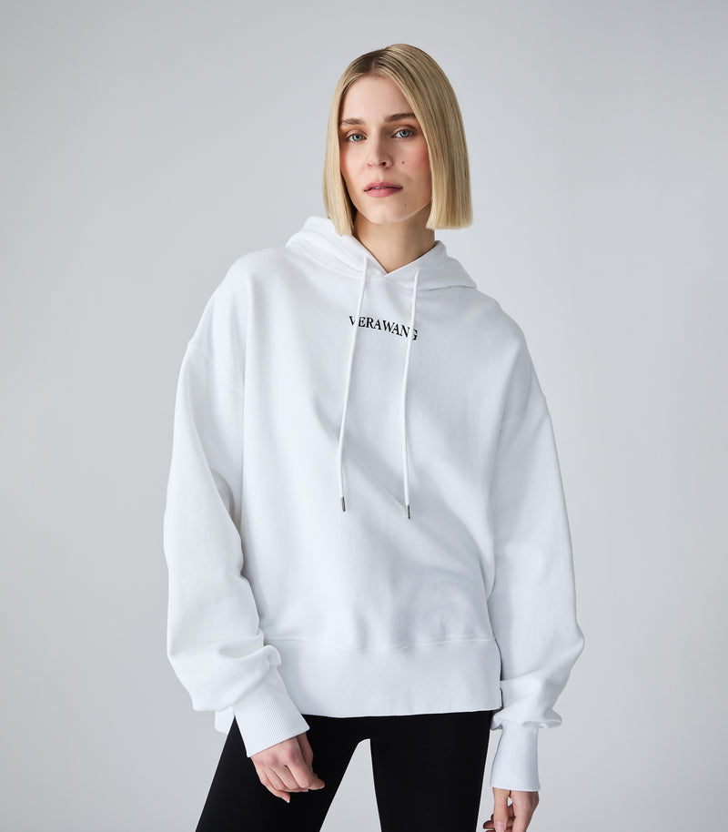 A blonde model wearing a white pullover hoodie with a black 