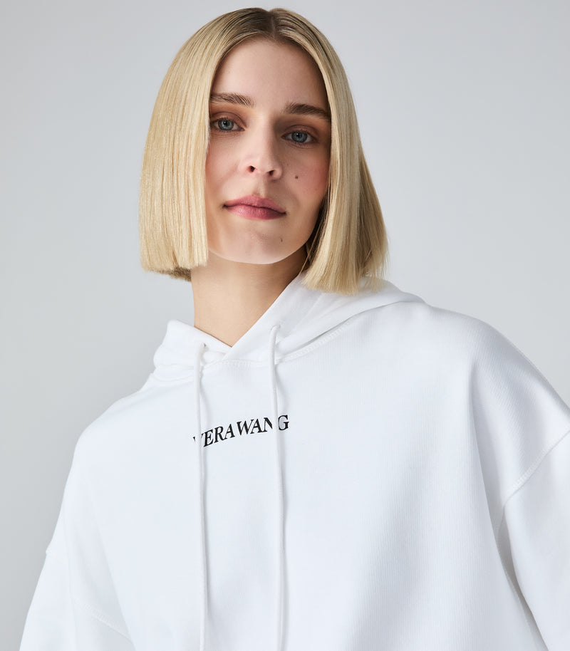 A blonde model wearing a white pullover hoodie with a black 