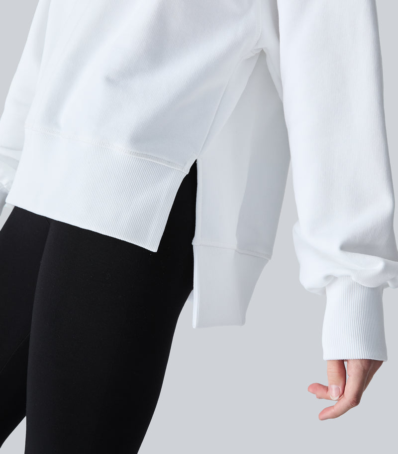 Close-up of a person wearing a white cropped sweatshirt with ribbed cuffs and hem, paired with black leggings, against a light gray studio background.