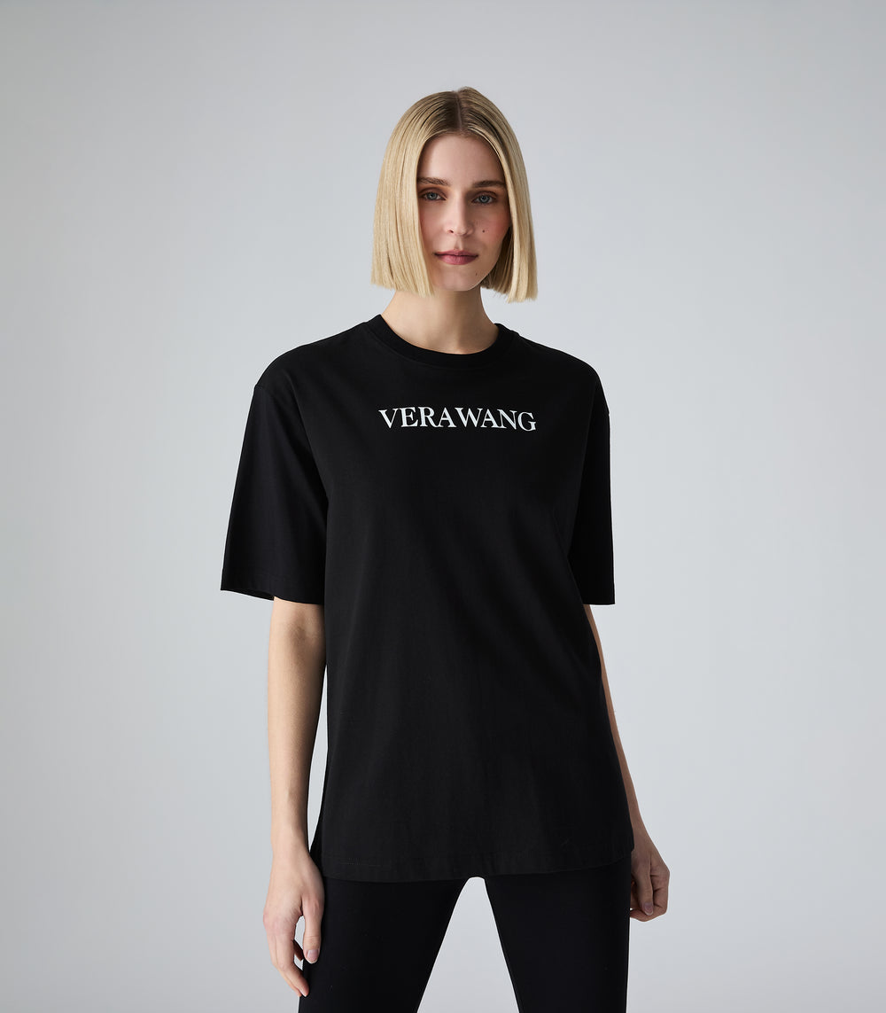 Half-length view of a model wearing a loose-fit black crewneck t-shirt featuring 'VERA WANG' spell-out logo in white lettering across the chest. The t-shirt is styled with black leggings against a white background.